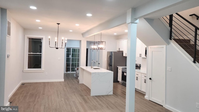 kitchen with pendant lighting, stainless steel appliances, white cabinetry, and an island with sink