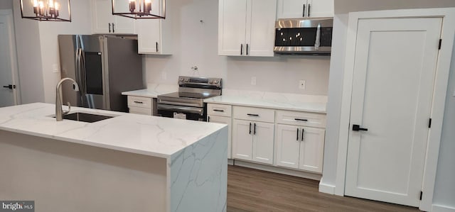 kitchen with light stone countertops, stainless steel appliances, hanging light fixtures, and an island with sink