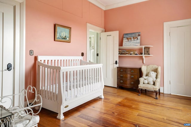 bedroom with hardwood / wood-style floors, crown molding, and a nursery area