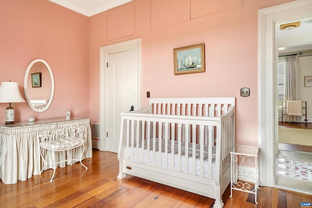 bedroom featuring ornamental molding, a nursery area, and wood-type flooring