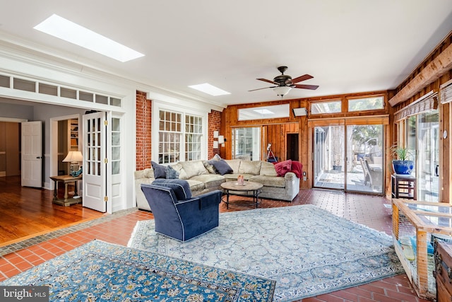 living room featuring a skylight, dark hardwood / wood-style floors, ceiling fan, brick wall, and ornamental molding