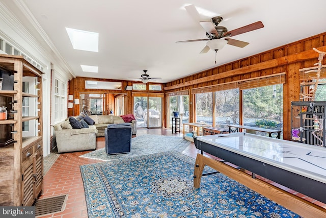 interior space featuring ornamental molding, ceiling fan, wood walls, and a skylight