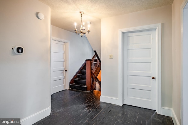 entrance foyer with a textured ceiling, a notable chandelier, and dark wood-type flooring