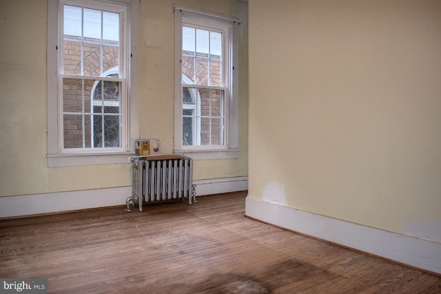 empty room with a healthy amount of sunlight, wood-type flooring, and radiator