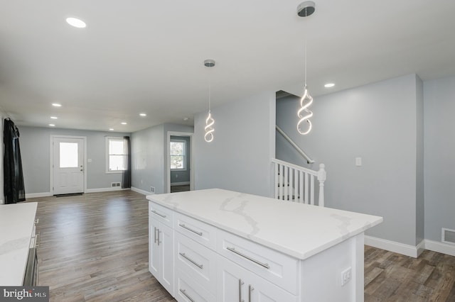 kitchen featuring light stone countertops, a center island, pendant lighting, white cabinets, and dark hardwood / wood-style flooring