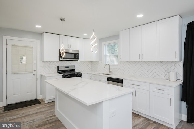 kitchen with appliances with stainless steel finishes, white cabinets, hardwood / wood-style flooring, and a center island