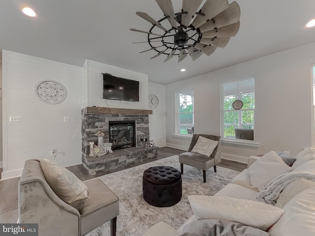 living room featuring a stone fireplace, wood-type flooring, and ceiling fan