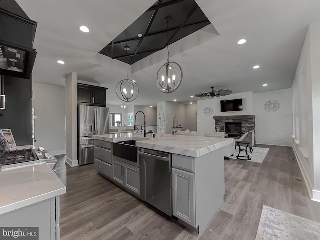 kitchen featuring sink, hanging light fixtures, stainless steel appliances, light stone countertops, and a center island with sink