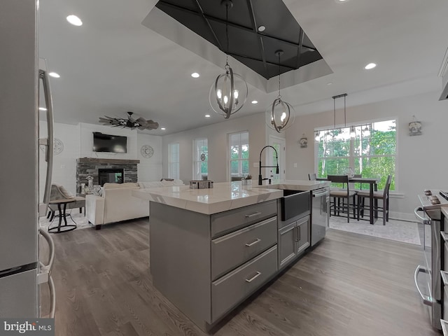 kitchen with gray cabinets, pendant lighting, a kitchen island with sink, stainless steel appliances, and light stone countertops