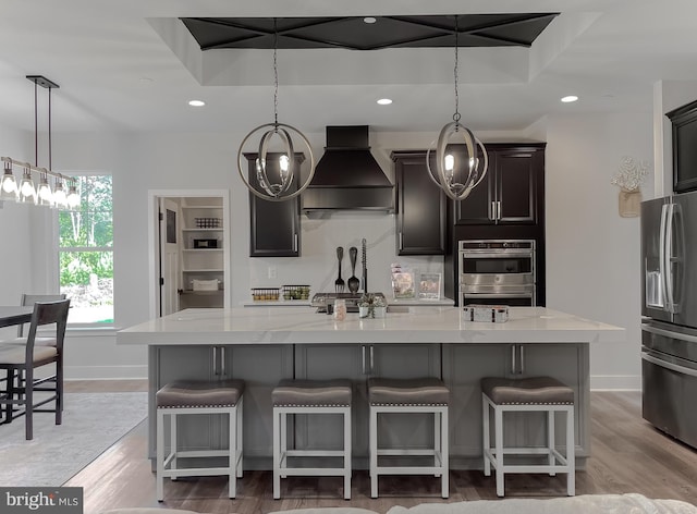 kitchen featuring a breakfast bar, custom exhaust hood, hanging light fixtures, a large island, and stainless steel refrigerator with ice dispenser