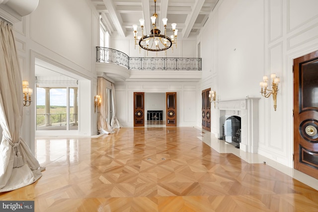 unfurnished living room featuring a towering ceiling, a fireplace, beamed ceiling, coffered ceiling, and a notable chandelier