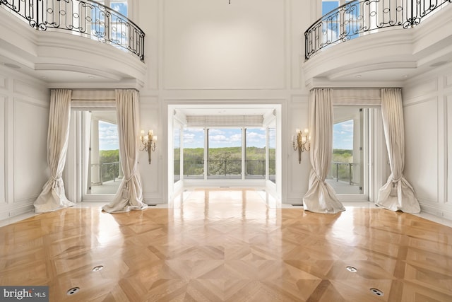 interior space with parquet floors, a towering ceiling, and a healthy amount of sunlight