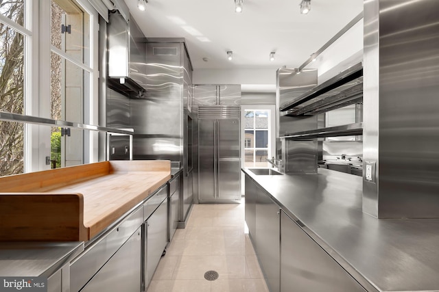 kitchen featuring sink, refrigerator, stainless steel counters, light tile patterned floors, and stainless steel built in fridge