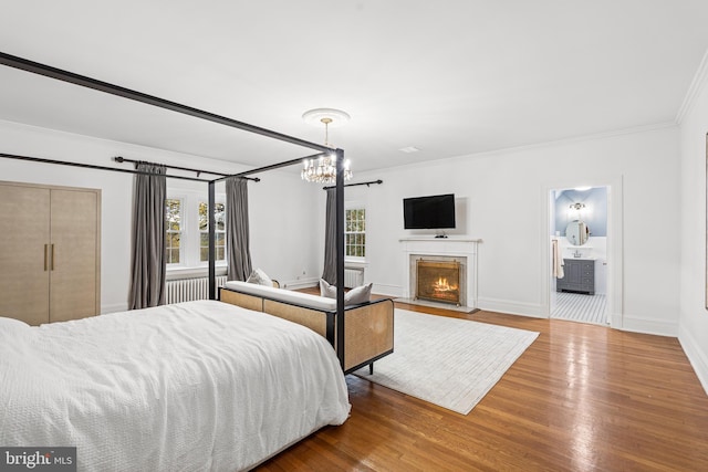 bedroom with ensuite bathroom, wood-type flooring, radiator, crown molding, and an inviting chandelier