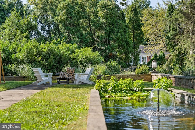 view of community with a water view, an outdoor fire pit, and a lawn