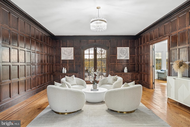 living room featuring french doors, wooden walls, ornamental molding, a notable chandelier, and light wood-type flooring