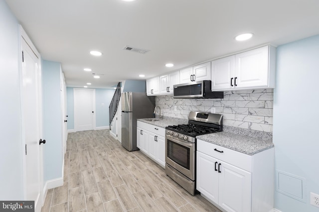 kitchen with light stone counters, stainless steel appliances, backsplash, light hardwood / wood-style floors, and white cabinets