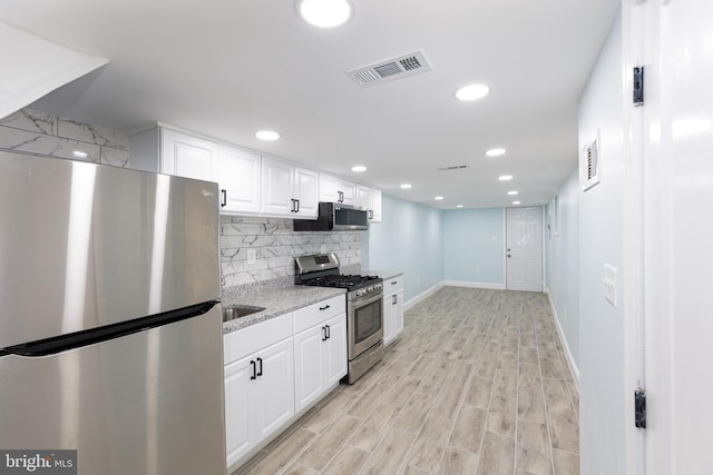 kitchen with appliances with stainless steel finishes, light hardwood / wood-style floors, white cabinetry, light stone countertops, and backsplash