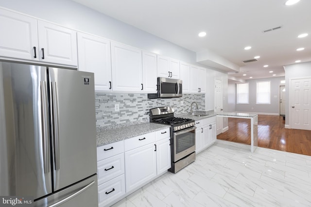 kitchen featuring white cabinetry, stainless steel appliances, light stone countertops, backsplash, and light tile flooring