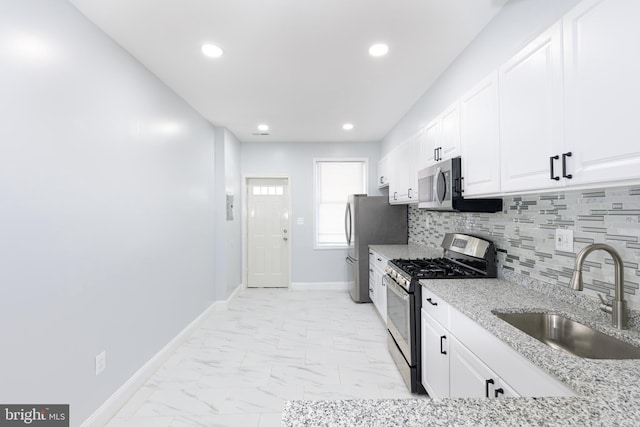 kitchen with white cabinetry, light tile flooring, appliances with stainless steel finishes, sink, and light stone counters