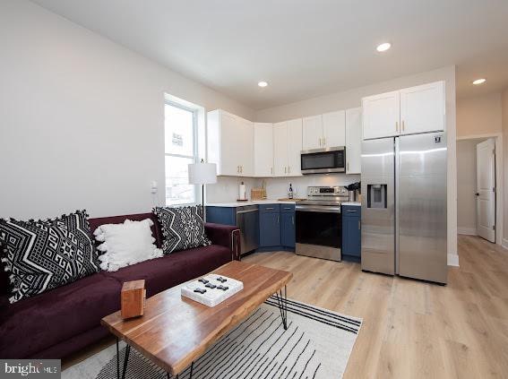 kitchen featuring white cabinets, blue cabinetry, stainless steel appliances, and light hardwood / wood-style floors