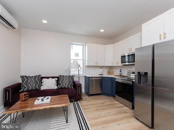 kitchen featuring blue cabinets, a wall unit AC, light wood-type flooring, white cabinets, and stainless steel appliances