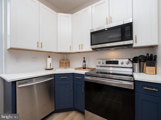 kitchen featuring appliances with stainless steel finishes, blue cabinetry, backsplash, light hardwood / wood-style floors, and white cabinetry