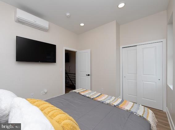 bedroom with a closet, an AC wall unit, and wood-type flooring