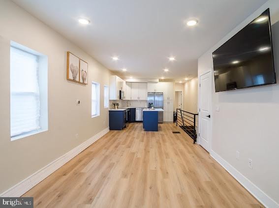 kitchen with white cabinets, a kitchen bar, stainless steel fridge, and light hardwood / wood-style flooring