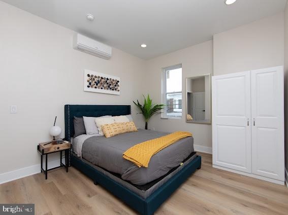 bedroom with light hardwood / wood-style floors and a wall mounted AC