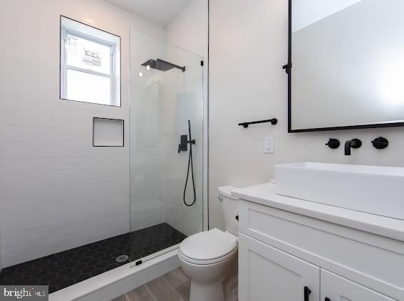 bathroom with hardwood / wood-style flooring, vanity, toilet, and tiled shower