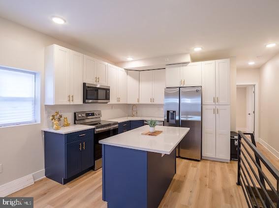 kitchen with light hardwood / wood-style flooring, stainless steel appliances, a kitchen island, and white cabinets