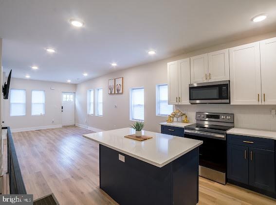 kitchen with backsplash, light hardwood / wood-style flooring, stainless steel appliances, white cabinets, and a kitchen island