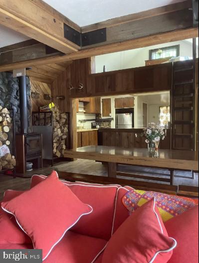 recreation room with wooden walls, a wood stove, beam ceiling, and hardwood / wood-style flooring