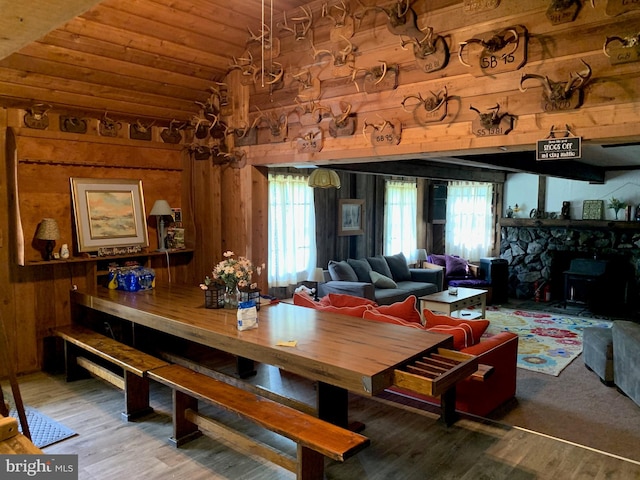 dining room featuring wood-type flooring, wooden walls, a fireplace, vaulted ceiling, and wood ceiling