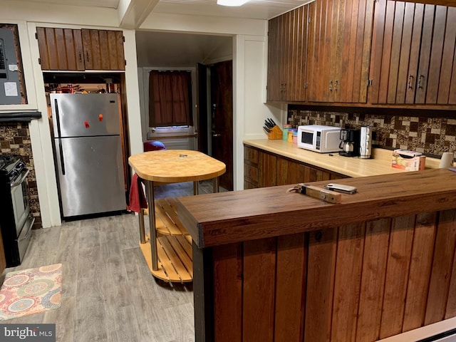 kitchen with backsplash, kitchen peninsula, appliances with stainless steel finishes, and light wood-type flooring