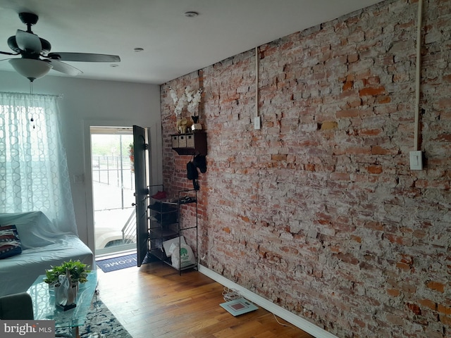 unfurnished living room featuring brick wall, hardwood / wood-style floors, and ceiling fan