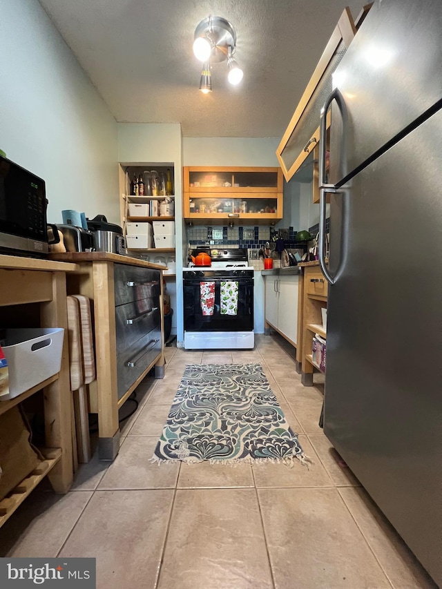 kitchen featuring white range with gas stovetop, light tile patterned floors, white cabinetry, and stainless steel refrigerator