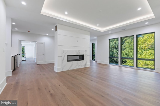 unfurnished living room with a tray ceiling, light hardwood / wood-style flooring, and a premium fireplace