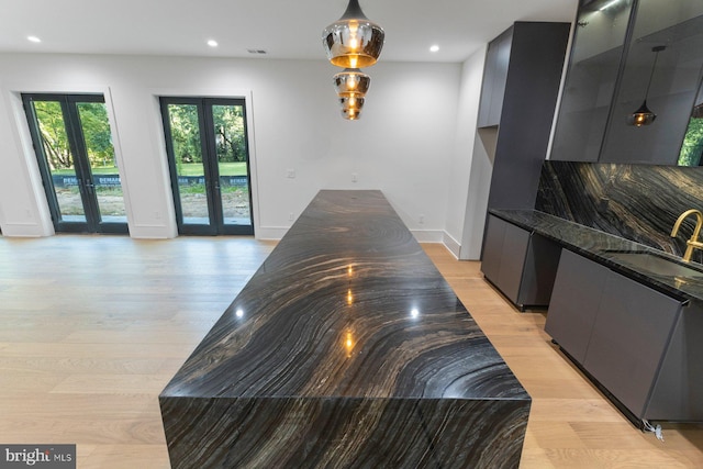 kitchen featuring light hardwood / wood-style floors, sink, dark stone countertops, french doors, and pendant lighting