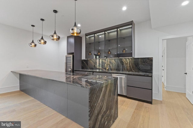 bar featuring stainless steel dishwasher, dark stone counters, hanging light fixtures, and light hardwood / wood-style floors