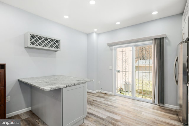 kitchen with kitchen peninsula, a kitchen bar, light wood-type flooring, light stone counters, and white cabinets