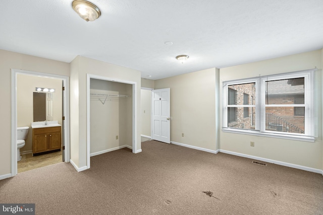 unfurnished bedroom featuring a closet, connected bathroom, light colored carpet, and sink