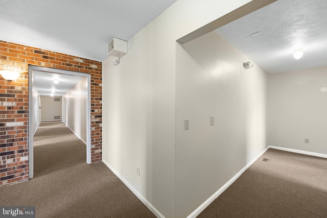 corridor with brick wall, dark colored carpet, and a textured ceiling