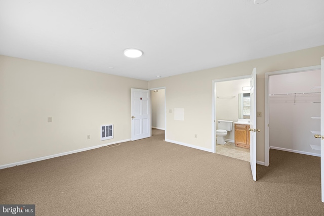 unfurnished bedroom with a closet, a walk in closet, ensuite bath, and light colored carpet