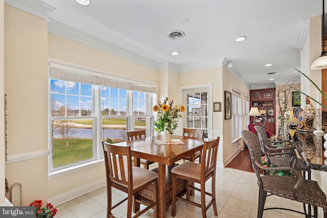 dining area with a water view, light tile floors, and crown molding