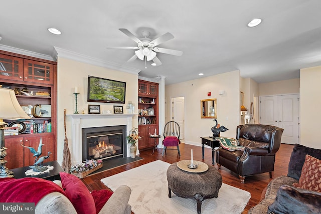 living room featuring built in shelves, ornamental molding, ceiling fan, and dark wood-type flooring