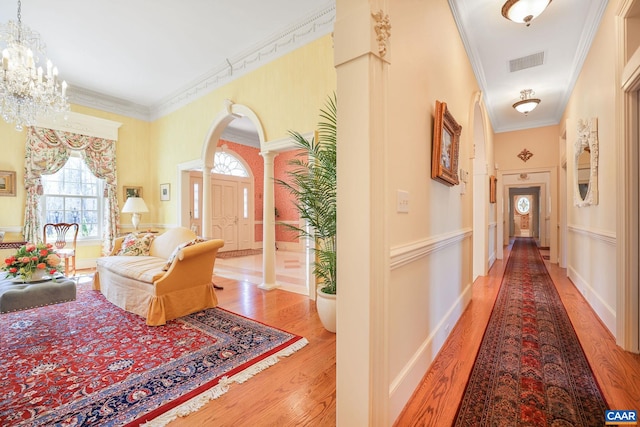 corridor with crown molding, decorative columns, light wood-type flooring, and an inviting chandelier