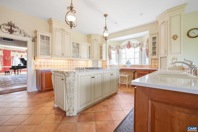 kitchen featuring decorative light fixtures, backsplash, sink, light tile floors, and a kitchen island