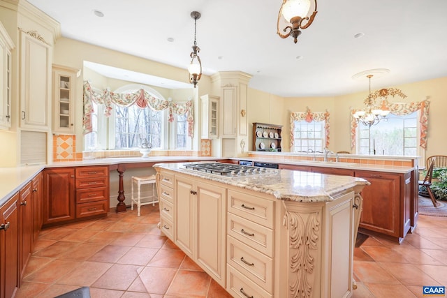 kitchen with a kitchen island, light tile floors, a notable chandelier, stainless steel gas cooktop, and pendant lighting